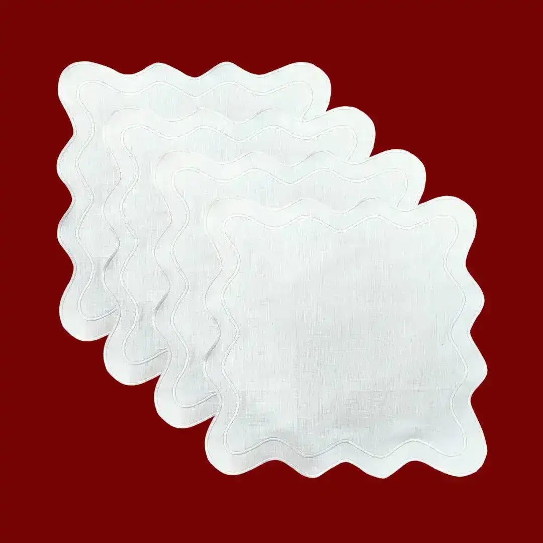 Stack of white scallop linen square placemats with wavy stitched border, fanned view on red background