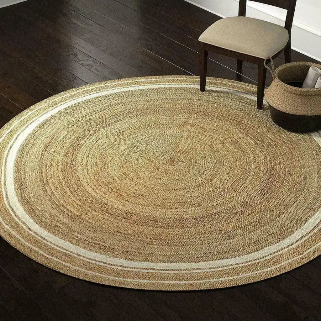 A beautifully crafted round area rug made from natural jute, featuring a white trim that adds a touch of elegance. This boho rug is perfect for a dining room setting, complementing the dark wooden floor and nearby chair. Ideal for formal dining rooms, this jute rug combines rustic charm with modern style.