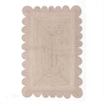 Top view of a Handmade Scalloped Jute Rug in soft white wash, 2 x 3 ft, with scalloped edges, placed in a living room setting.