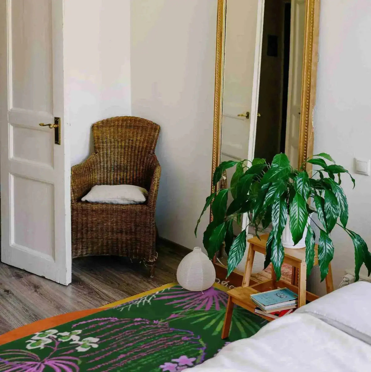A cozy living room setting featuring a Wild Bloom Elegant Hand Tufted Wool Area Rug. The vibrant design of the wool rug complements the natural decor, with a wicker chair, a large mirror, and a lush plant adding to the room's inviting atmosphere. Perfect for office or living room use.
