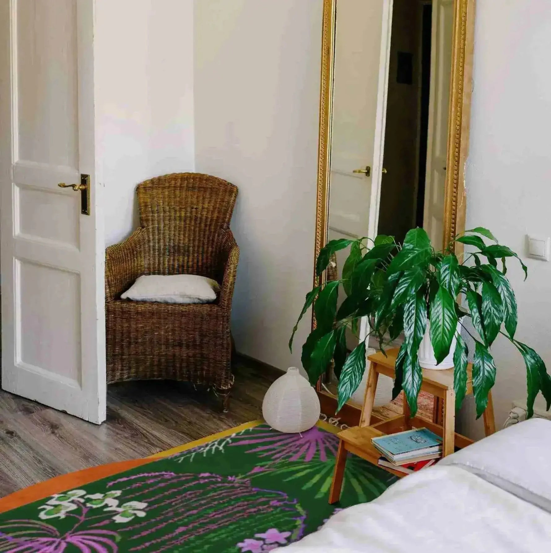 A cozy living room setting featuring a Wild Bloom Elegant Hand Tufted Wool Area Rug. The vibrant design of the wool rug complements the natural decor, with a wicker chair, a large mirror, and a lush plant adding to the room's inviting atmosphere. Perfect for office or living room use.