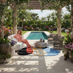 Woman sitting on a white chair by a pool with a colorful rug and decorative elements.