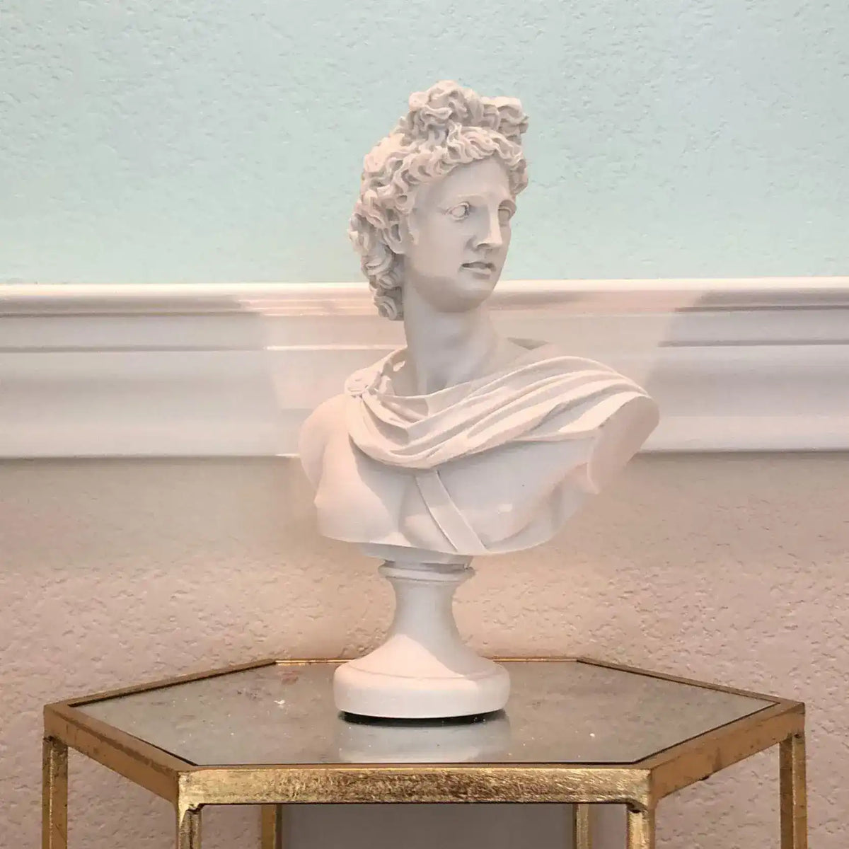White Apollo Belvedere bust on a gold mirrored hexagonal table, showing the sculpted toga drape