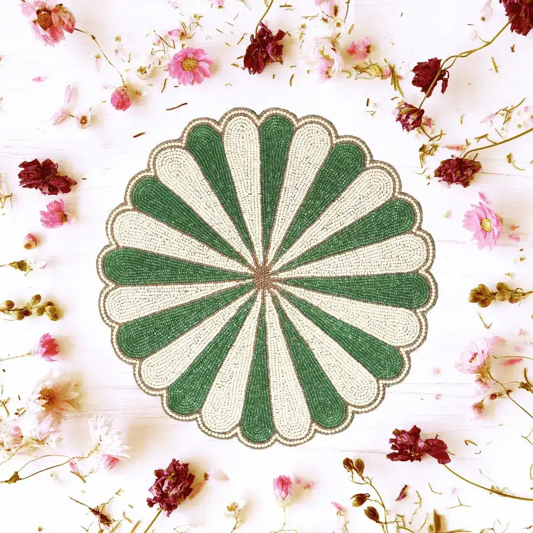 Green and white beaded scallop round placemat surrounded by scattered dried red and pink flowers on white flat-lay