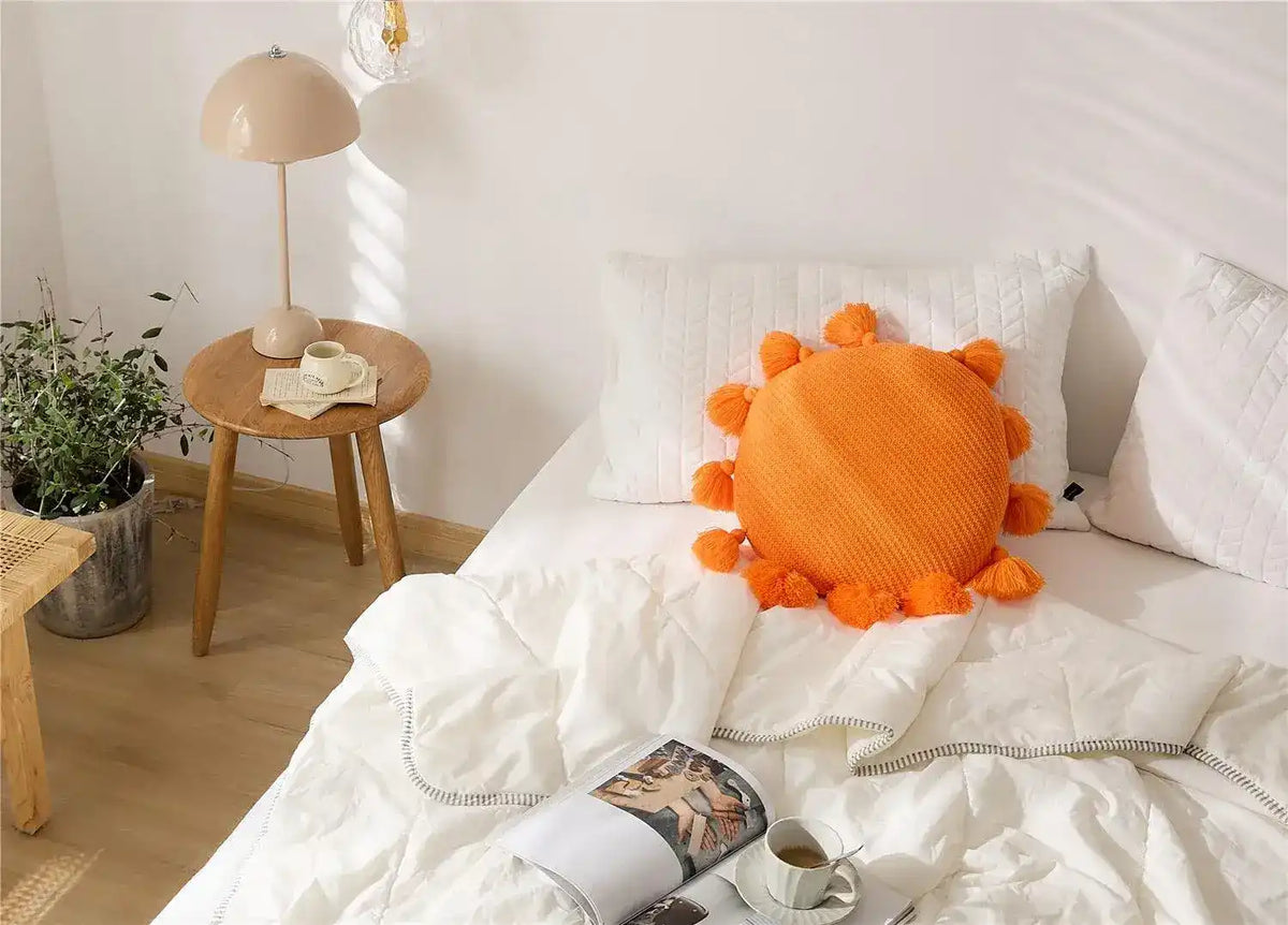 Round decorative throw pillow with tassels in vibrant orange color, adding a cheerful touch to a modern bedroom decor.