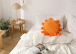 Round decorative throw pillow with tassels in vibrant orange color, adding a cheerful touch to a modern bedroom decor.