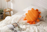 Round tassel decorative throw pillow in vibrant orange, placed on a neatly made bed with white bedding and a cozy atmosphere.