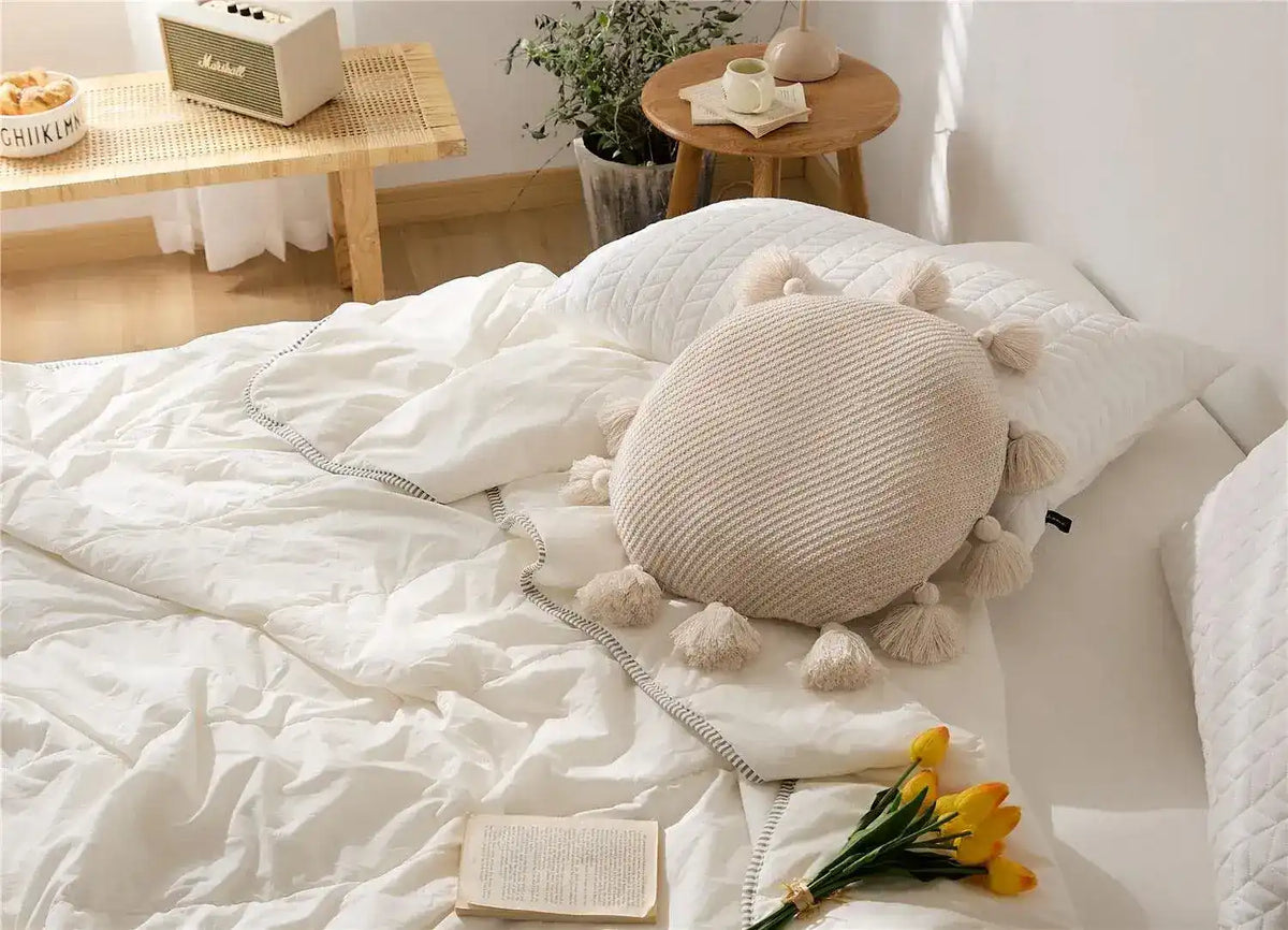 Round tassel decorative throw pillow on a bed with white bedding, adding a cozy and stylish touch to the decor.
