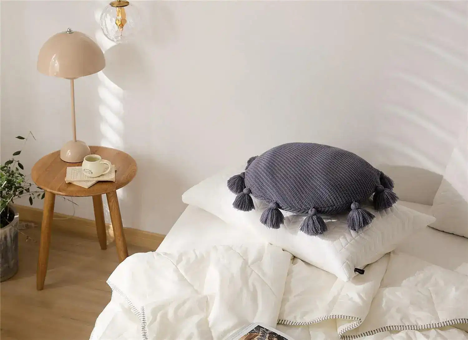 Round decorative throw pillow with tassels placed on a bed, enhancing the cozy interior decor.